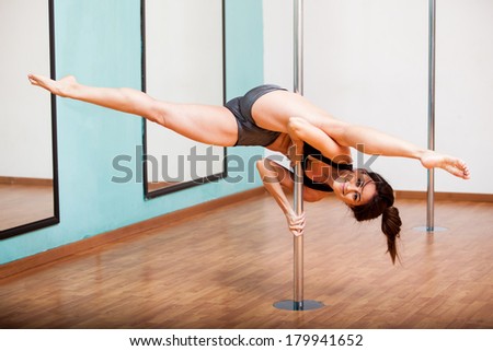 Strong and flexible young woman splitting her legs while hanging on from a pole