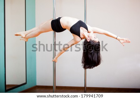 Pretty Hispanic girl holding the reverse superwoman pose in a pole fitness class