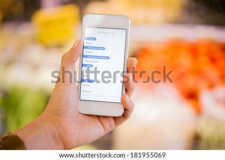 Closeup of a woman\'s hand holding a smart phone with a shopping list at a grocery store