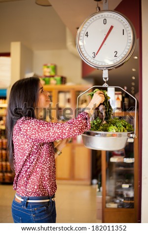Beautiful girl weighing some vegetables on a scale at the grocery store