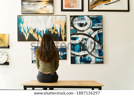 Young female visitor looking reflective while sitting on a bench and admiring the various paintings on the wall of an art gallery Foto d'archivio © 