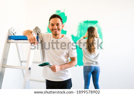 Handy husband painting the walls with a paint roller along her loving wife. Married couple redecorating and remodeling their new house Foto stock © 
