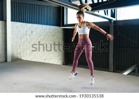 Strong young woman in activewear jumping in a cardio workout at the gym. Beautiful latin woman doing burpees during a HIIT training
