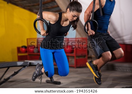Athletic man and woman doing some pull up exercises in the gymnastic rings in a gym