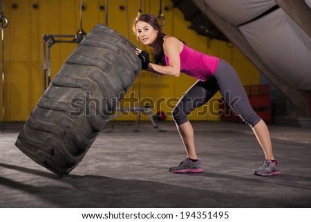 Pretty brunette working out with a big tire in a gym