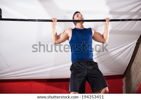 Strong Hispanic man doing some pull ups in a bar at a gym