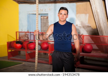 Strong young man about to climb a rope as part of the workout of the day in a cross-training gym