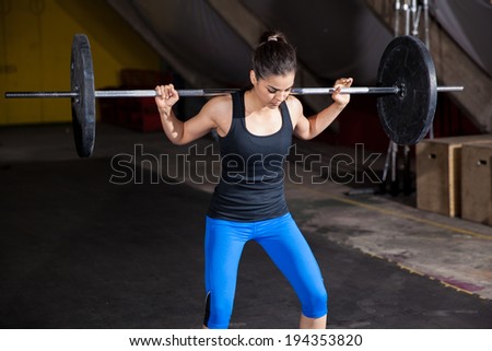 Pretty girl doing some squats with a barbell in a gym