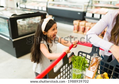 Angry little kid screaming and throwing a tantrum while grocery shopping with her mom at the supermarket because she won't buy her candy