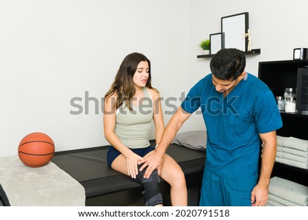 I'm in so much pain. Stressed young woman with a leg brace suffering from a sports injury. Physical therapist talking with a patient  Stock fotó © 