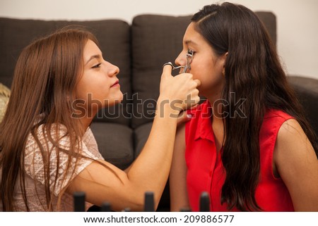 Cute teenage brunette using an eyelash curler on her best friend