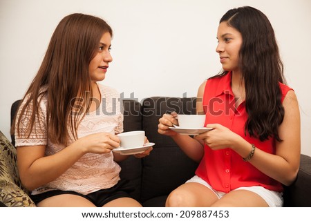 Cute female teenage friends chatting and drinking coffee at home