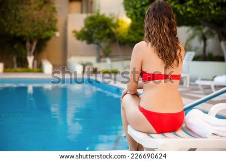 Rear view of a pretty young brunette wearing a bikini and sitting on a poolside chair