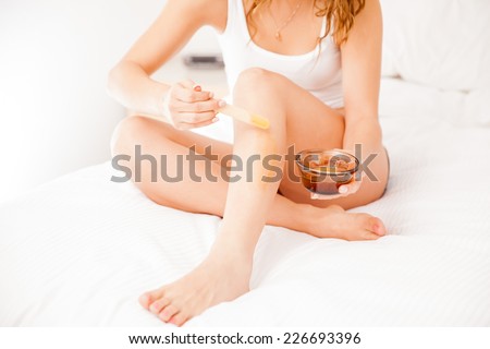 Young woman spreading some wax on her legs with a stick to remove her hair