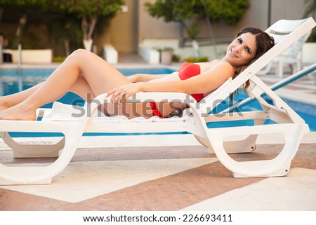 Pretty young Hispanic woman wearing a bikini by the pool and smiling