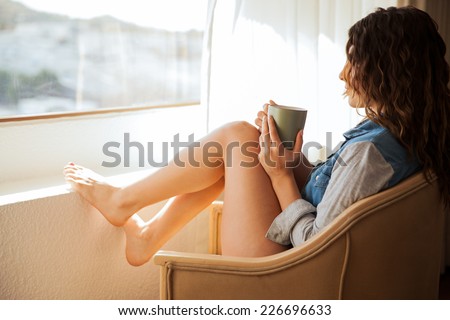 Beautiful young brunette in underwear sitting next to a window and enjoying a cup of coffee in the morning
