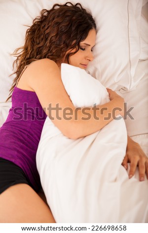 Pretty Hispanic young woman sleeping on her side on a bed and hugging a pillow