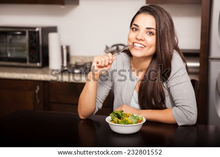 Beautiful young brunette biting her fork while eating a healthy salad at home