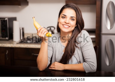 Gorgeous young woman about to eat a banana at home and smiling