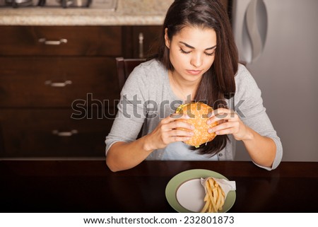 Top view of a young woman eating a cheeseburger and french fries at home