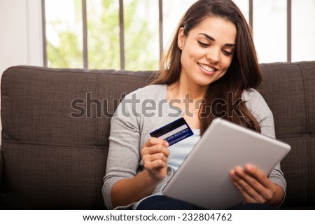 Cute young woman shopping online with her credit card and a tablet computer at home