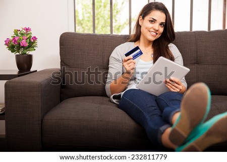 Beautiful young Latin woman using her credit card and tablet computer to purchase some stuff online