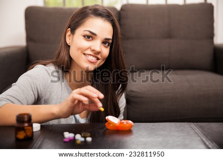 Pretty young Hispanic brunette using a pill organizer to sort her vitamins out at home