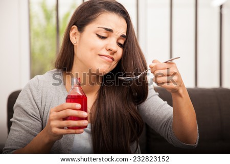 Young woman making a face of disgust at a spoon full of cough syrup