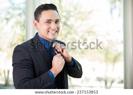 Portrait of a young Hispanic businessman fixing his tie and smiling
