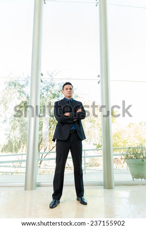 Portrait of a young man in a suit standing inside a large office
