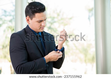 Portrait of a young Latin businessman fixing her suit and sleeves before going on a job interview