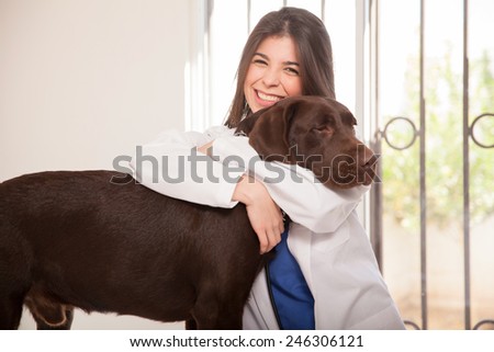 Portrait of a pretty veterinarian in a lab coat hugging a big dog in her clinic and smiling
