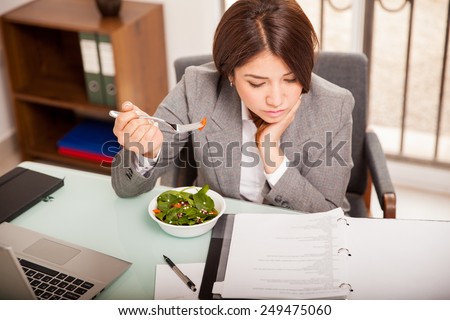 Busy young business woman eating a healthy lunch while working in her office