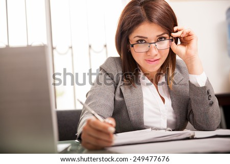Cute Latin business woman flirting and playing with her glasses while working in her office