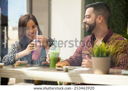 Cheerful young couple having lunch and healthy smoothies at a juice bar