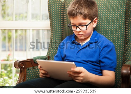Pretty young boy with glasses watching a movie on a tablet computer at home