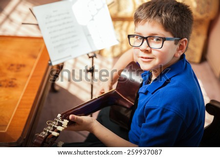 Portrait of a young boy with glasses practicing a song during a guitar lesson at home