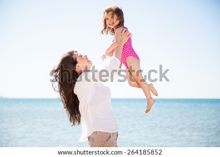 Happy young Latin mother lifting her daughter up in the air on a sunny day at the beach