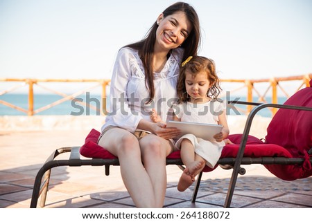 Portrait of a beautiful Hispanic mother and her daughter playing games on a tablet computer while relaxing at the beach