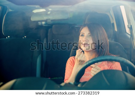Reckless young woman putting some lipstick on while driving a car. Shot through the windshield