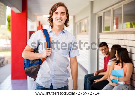 Portrait of a young man standing in a university hallway and smiling next to some of his friends