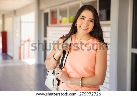 Portrait of a beautiful young Latin college student with a backpack standing in a school hallway