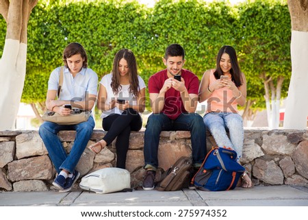 Group of young adults using their smartphones at school