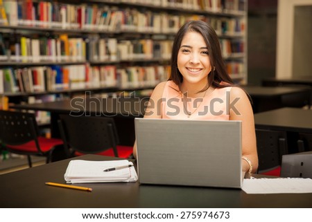 Portrait of a young brunette using a laptop computer for school work in the library and smiling