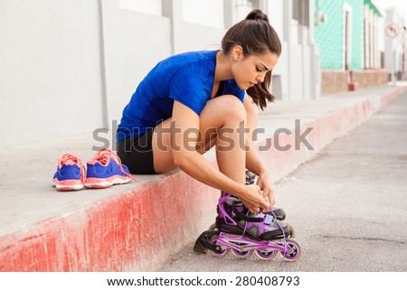Profile view of a woman sitting on the sidewalk and putting her inline skates on