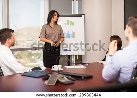 Pretty young woman giving a sales pitch to a group of business people in a meeting room