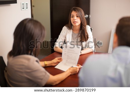 Portrait of a young Hispanic woman sitting in front of two people during a job interview