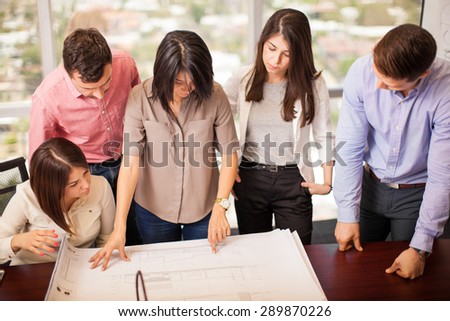 Group of five young architects working and looking at a building plan in a meeting room