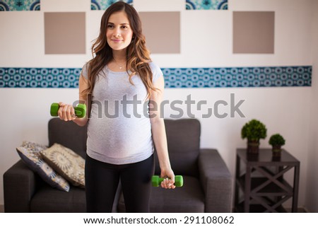 Cute young pregnant woman working out with a couple of dumbbells at home