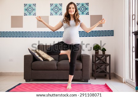 Beautiful young pregnant brunette doing some yoga poses in the living room